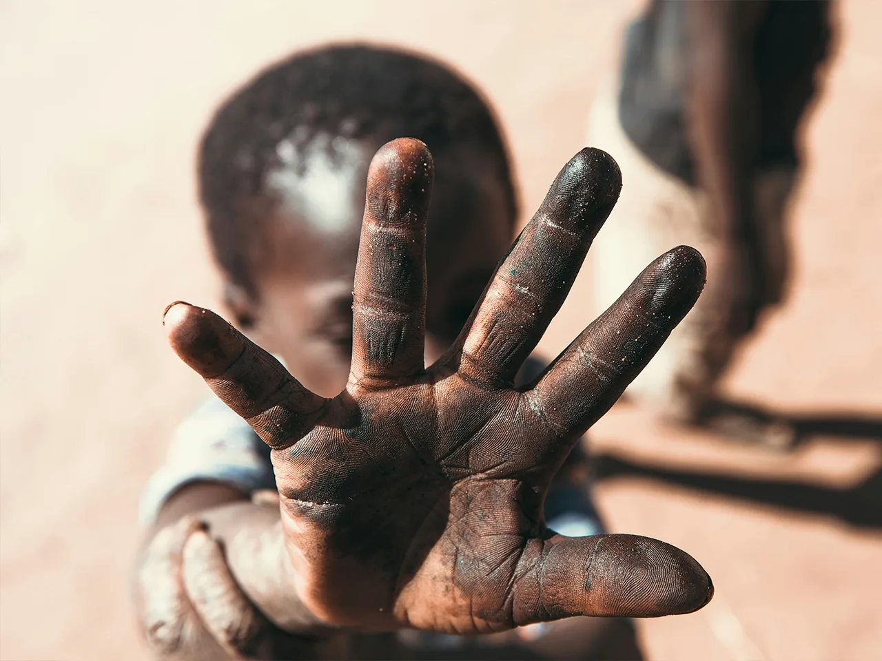 A young child reaches out an open, dust-covered hand toward the camera.